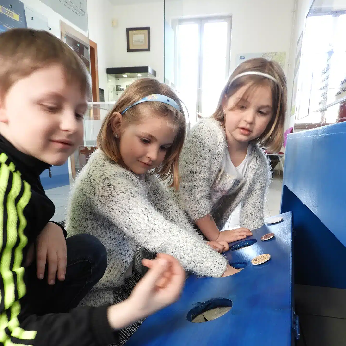 Image de 3 jeunes enfants participant à l'atelier des sens des p’tits mouss. Ils plongent leurs mains dans des bacs pour découvrir des matières.